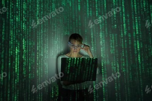 Preview: Confident woman adjusting futuristic glasses while using laptop against dark background