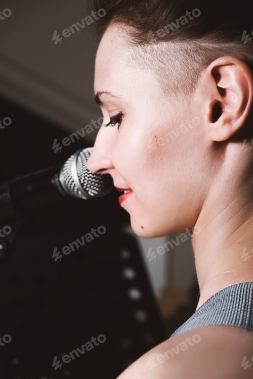 Preview: young female rock singer with microphone, smiling and singing. rear view.