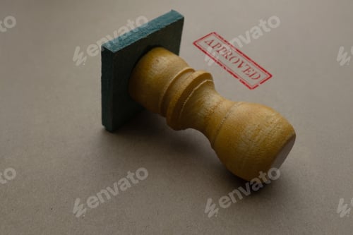 Preview: Close-up of a wooden rubber stamp with a red APPROVED mark on brown paper.