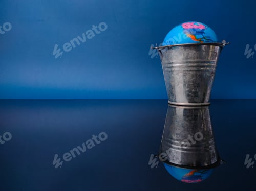 Preview: Earth globe in a steel bucket with reflection on a black acrylic board
