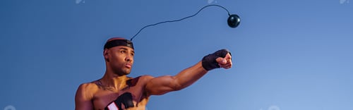 Preview: Sporty man with naked torso uses a boxing ball simulator for training on studio background