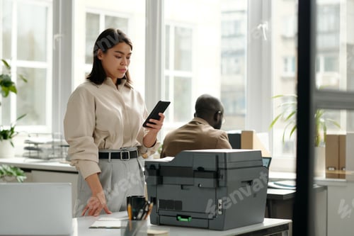 Preview: Young serious businesswoman looking at smartphone screen in office