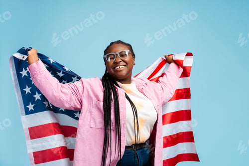 Preview: Excited beautiful African American woman, patriot wearing glasses holding American flag