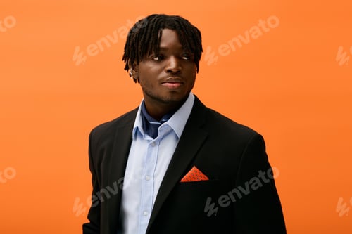 Preview: Handsome young man in stylish attire poses confidently against a vibrant orange backdrop