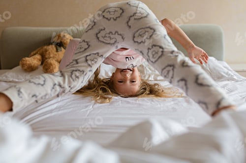 Preview: Happy little Caucasian girl with blonde hair playing on bed at home