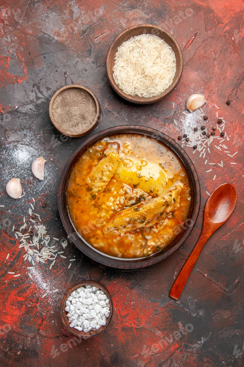 Preview: top view chicken soup bowls with pepper rice sea salt garlic spoon on dark red background