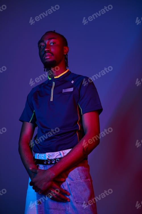 Preview: Young African American man in stylish attire poses confidently under vibrant neon lights