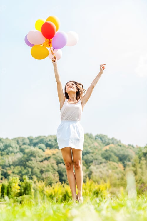 Preview: Flying away. Happy young woman holding colorful balloons and flying over a green meadow