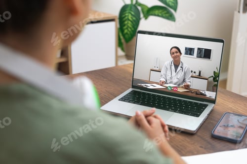 Preview: Over-the-shoulder view of a patient having a video call with a smiling doctor on laptop