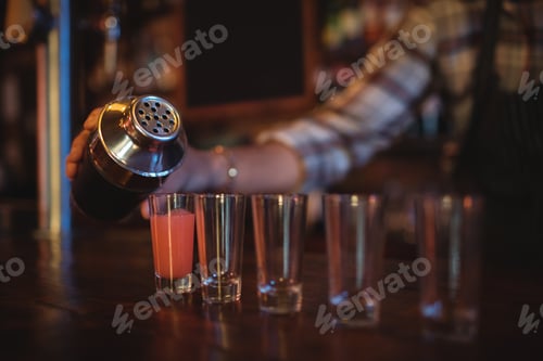 Preview: Waiter pouring cocktail drink into shot glasses at counter