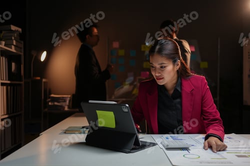 Preview: Dedicated female professional working late in dimly lit office using digital tablet