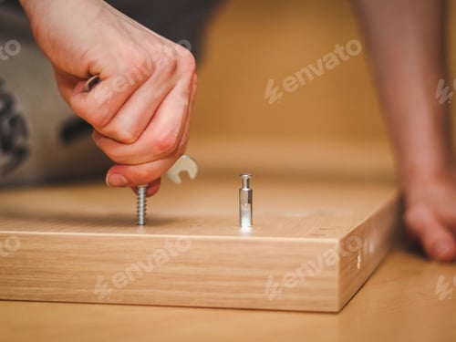 Preview: The hands of a Caucasian young man twist a bolt on the wooden part of the bed