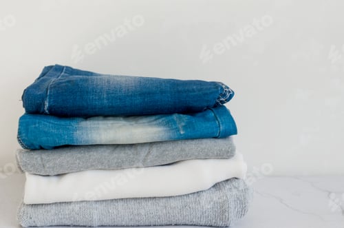 Preview: Stack of sweaters and blue jeans on grey background,