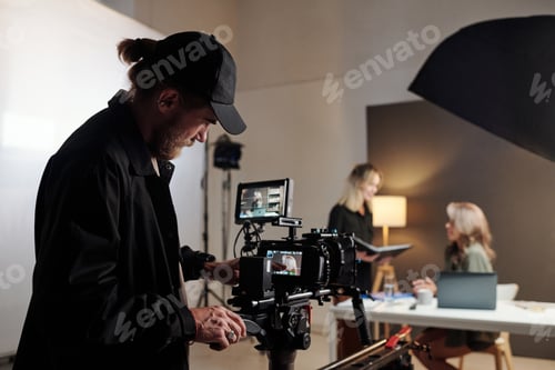 Preview: Young serious production studio worker adjusting videocamera during shooting