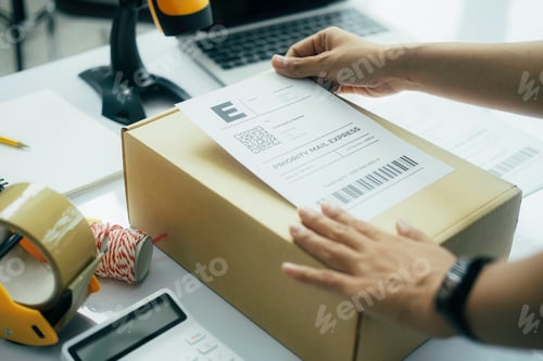 Preview: Young business owner putting shipping label on parcel.