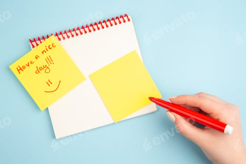 Preview: top view spiral notebook red marker in woman hand have a nice day written on yellow note paper on