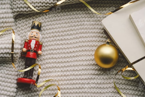 Preview: A nutcracker and golden ornament on a cozy knitted blanket during the holiday season