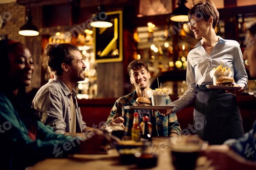 Preview: Happy waitress serving food to group of guests in a pub.