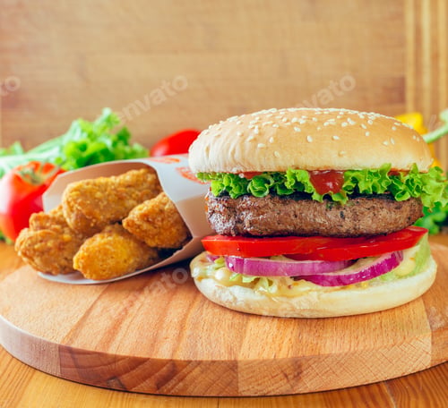 Preview: Delicious burger with fresh toppings alongside crispy chicken pieces on a wooden surface