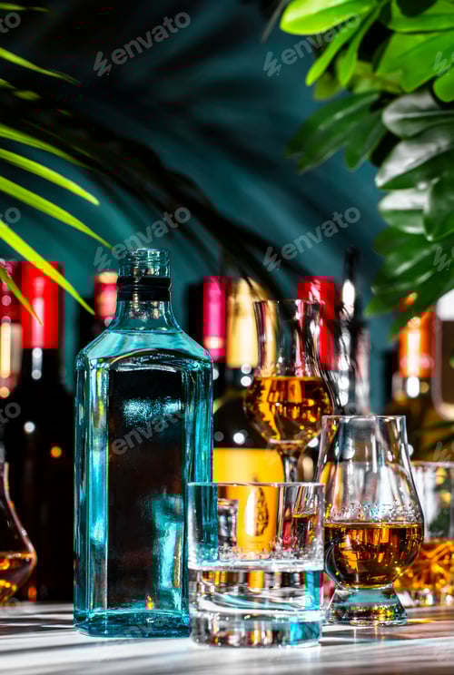 Preview: Dry gin in glass with sapphire blue bottle and strong drinks bottles on dark green background