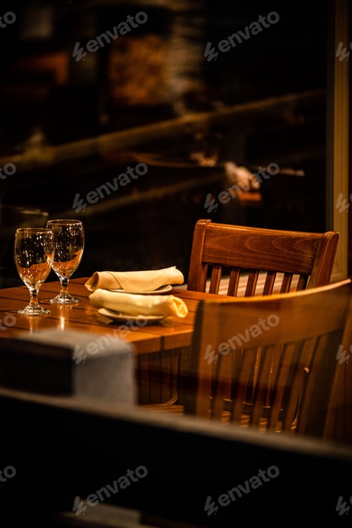 Preview: Vertical of empty wine glasses and nicely folded serviettes on a wooden table set for two