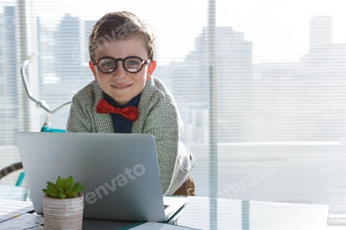 Preview: Boy student leaning forward over desk by office windows working on laptop near bicycle