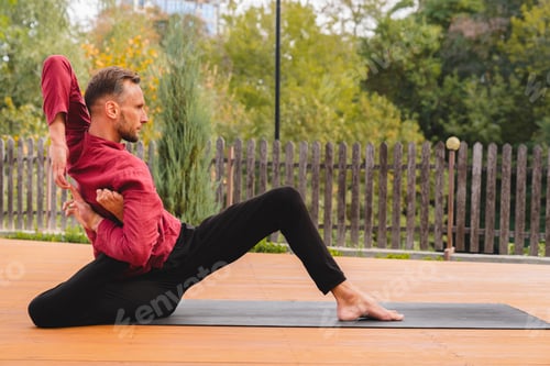 Preview: Side view shot of 30s flexible male yogi doing yoga exercises on mat in the garden