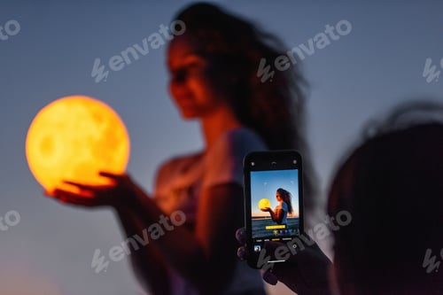 Preview: Friend takes phone photo of sister holding the moon in hands. Girls make social media content