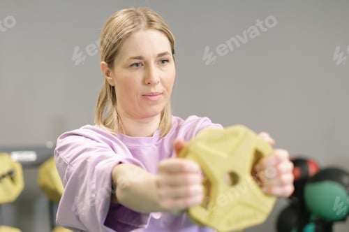 Preview: blond Woman holding a lightweight disk for working out arms and triceps in gym.