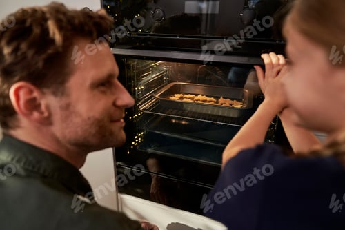 Preview: Back view of caucasian father and daughter waiting for homemade cookies