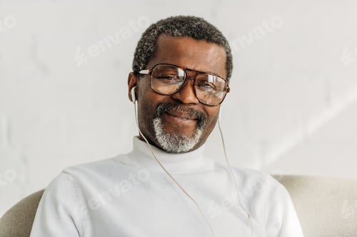 Preview: stylish, senior african american man in glasses listening music in earphones and smiling at camera
