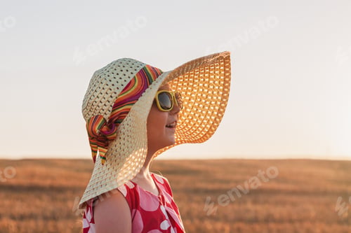Preview: Child girl in straw hat dress in wheat spikelets field. Smiling kid in sunglasses on sunset