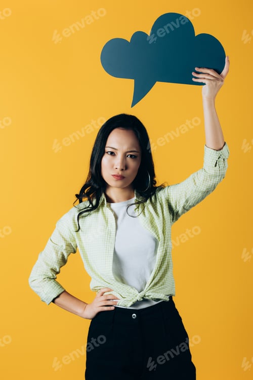 Preview: upset asian woman holding speech bubble, isolated on yellow