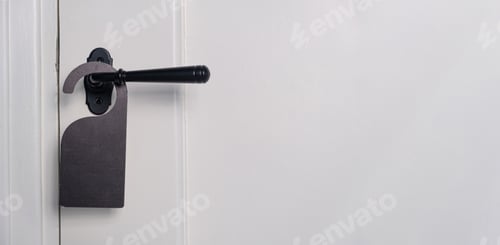 Preview: Hotel room hanger blank, empty for your text. Black label on closed door knob, close up view.