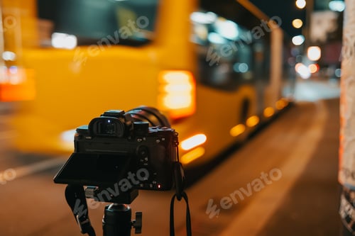 Preview: Digital modern camera filming a busy night street in big city. Yellow bus passes by. Photography cit
