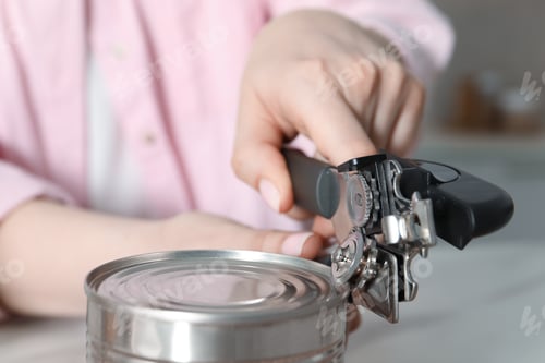 Preview: Woman opening tin with can opener at white table, closeup