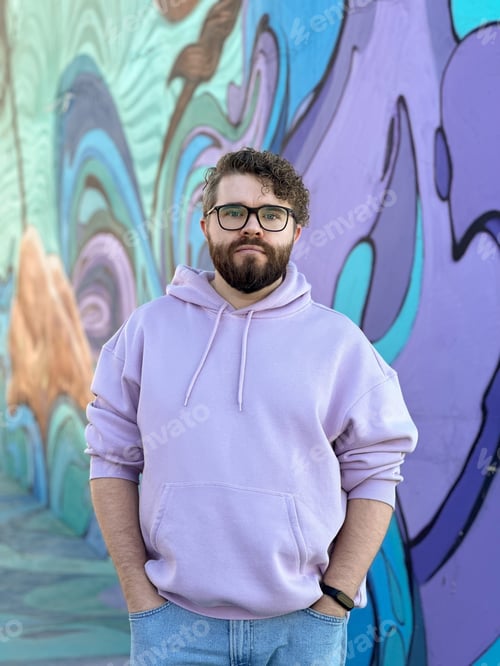 Preview: Millennial man in a pastel hoodie standing in front of a vibrant, abstract mural. Soft fabric and