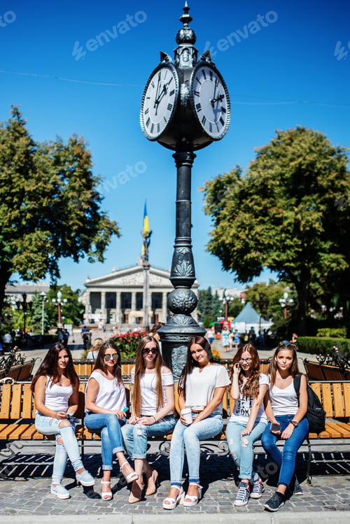 Preview: Six beautiful young girls sitting on a bench next to the old street clock in the park.