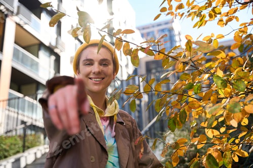 Preview: Smiling woman stands against backdrop of skyscraper, near autumn tree