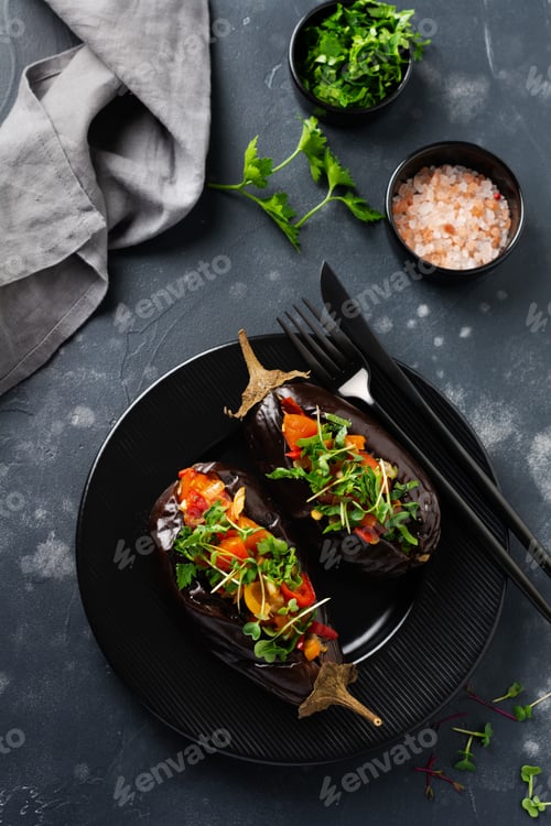 Preview: Baked stuffed eggplant with different vegetables, tomato, pepper, onion and parsley on a black stone