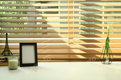 Preview: Blank picture frame, candle, books and flower pot on white table. Comfortable workplace.