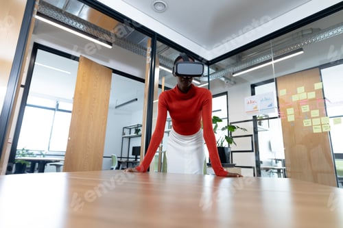 Preview: African american businesswoman leaning on desk and using vr headset in meeting room