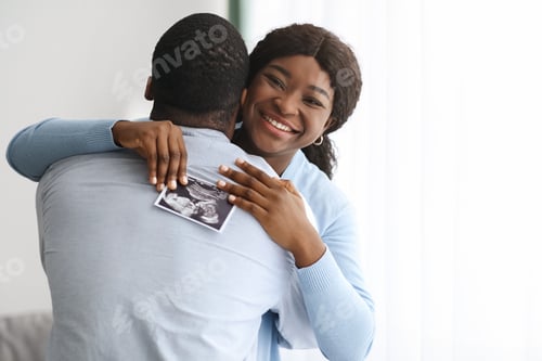 Preview: Emotional black woman holding ultrasound image and hugging her husband