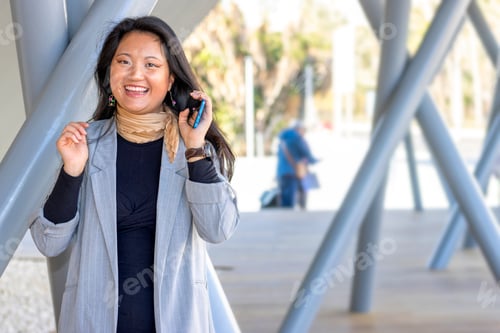 Visualização: Mulher de negócios asiática eufórica olhando para a câmera em uma estação de trem enquanto espera