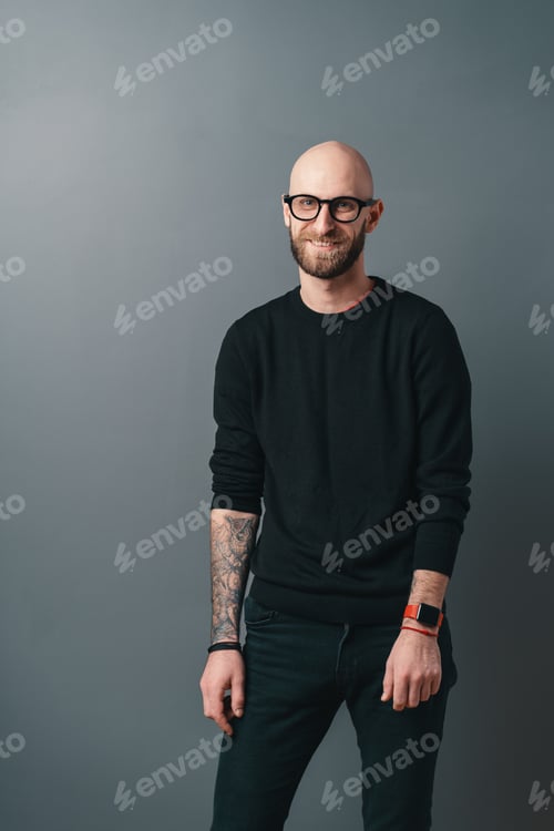 Preview: Young smiling man with beard and glasses on gray studio background