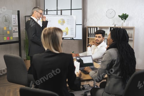 Preview: Male manager in business suit, speaking at office meeting with his multiethnic colleagues