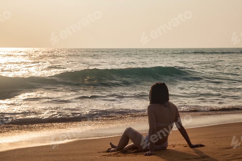 Preview: Silhouette of young slim woman sitting on tropical beach at sea sunse