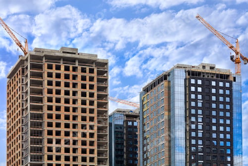 Preview: Low angle shot of modern buildings under construction under a bright blue sky