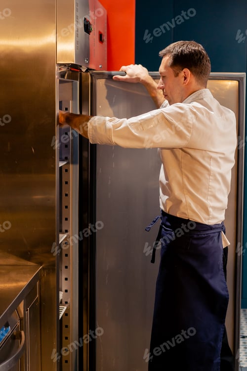 Preview: professional kitchen chef looks into the fridge and chooses ingredients for cooking food concept