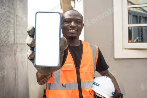 Preview: Young adult construction worker wearing an orange jacket and a white hard hat showing his phone